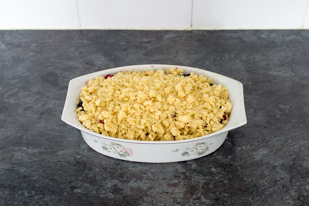 Summer fruits topped with homemade crumble mixture in a decorative dish.