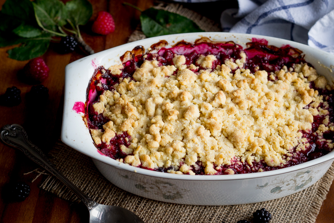 An apple berry crumble in a dish with a serving spoon to the side.
