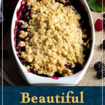 A decorative white dish filled with a bubbling Summer fruit crumble, set on hessian fabric with berries scattered around it. A text overlay says ""Beautiful Summer fruit crumble".