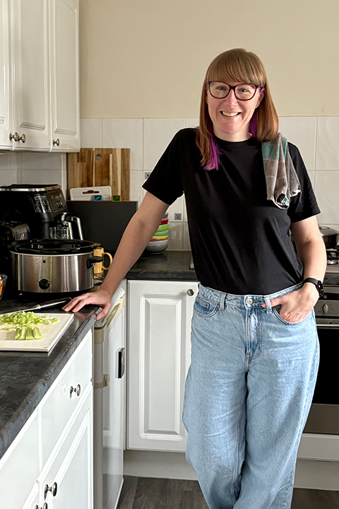 Emma smiling in her kitchen next to a slow cooker and chopping board filled with chopped vegetables.