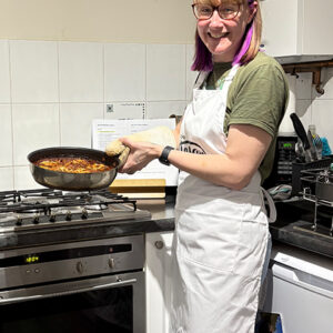 Emma holding a frying pan filled with a one-pot meal that she made on a cook-along with customers.