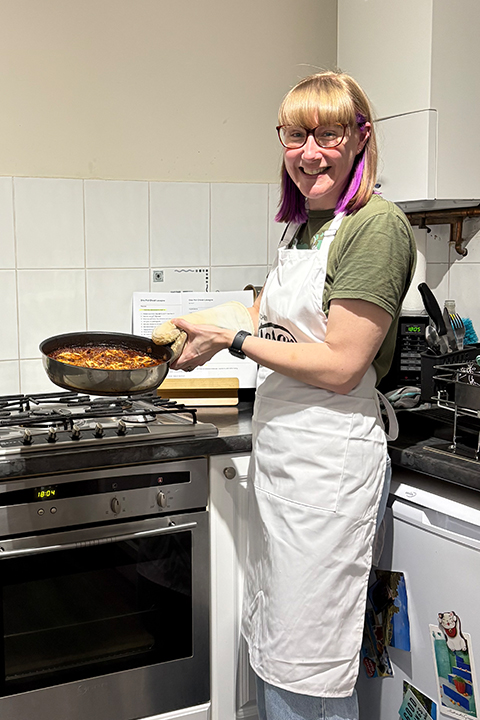 Emma holding a frying pan filled with a one-pot cheat lasagne that she made on a cook-along with customers.