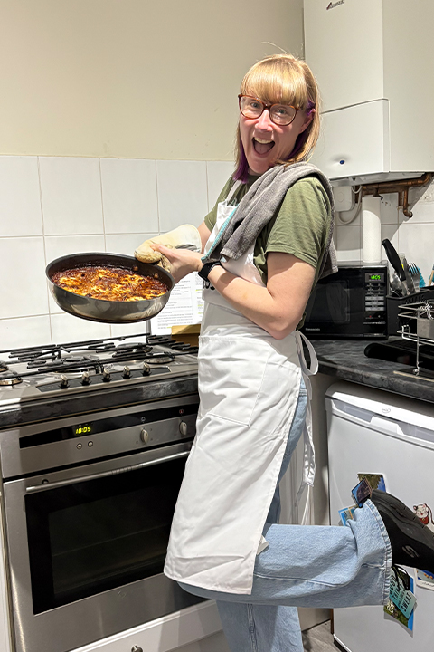 Emma smiling and holding a frying pan filled with a one-pot cheat lasagne that she made on a cook-along with customers.