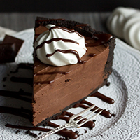 A slice of rich and decadent no bake chocolate cheesecake on a white plate with a fork.