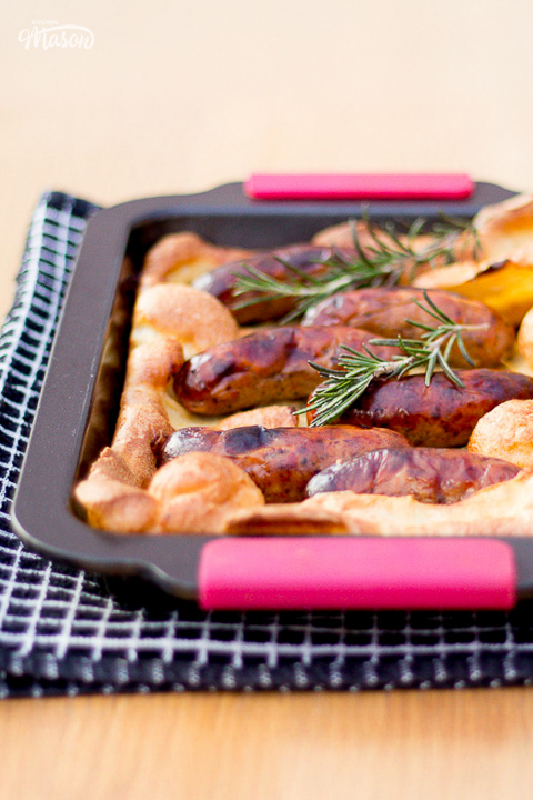 A golden toad in the hole topped with rosemary sprigs on a tea towel.