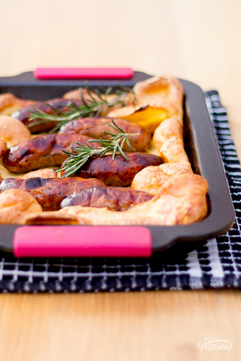 A light and fluffy toad in the hole in a roasting dish on a tea towel.