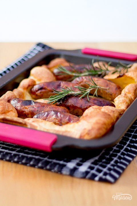 A well risen toad in the hole topped with rosemary set over a tea towel on a dining table.