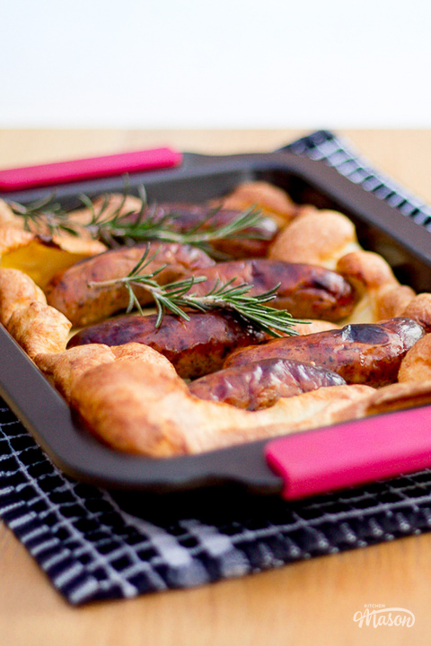 A perfectly golden toad in the hole in a roasting dish on a dining table.