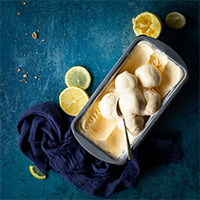 A loaf tin of homemade lemon ice cream with a spoon pushed into it.