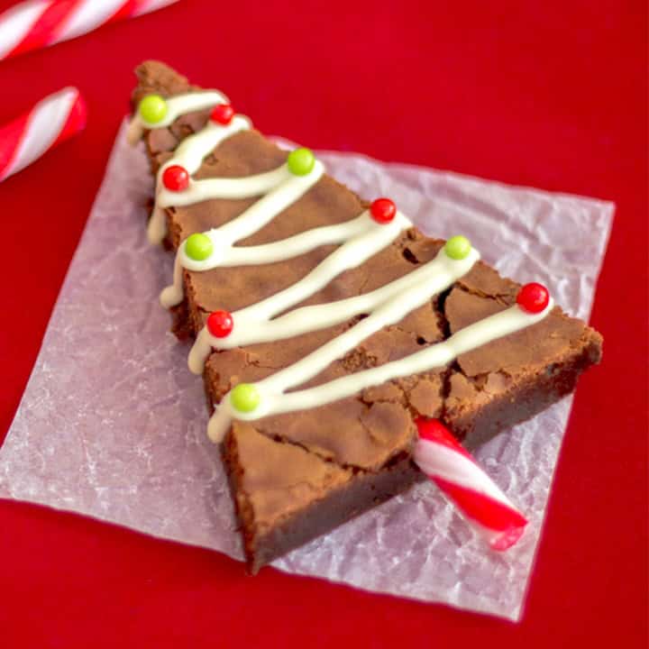 A Christmas tree brownie on a sheet of baking paper with candy canes at the side.