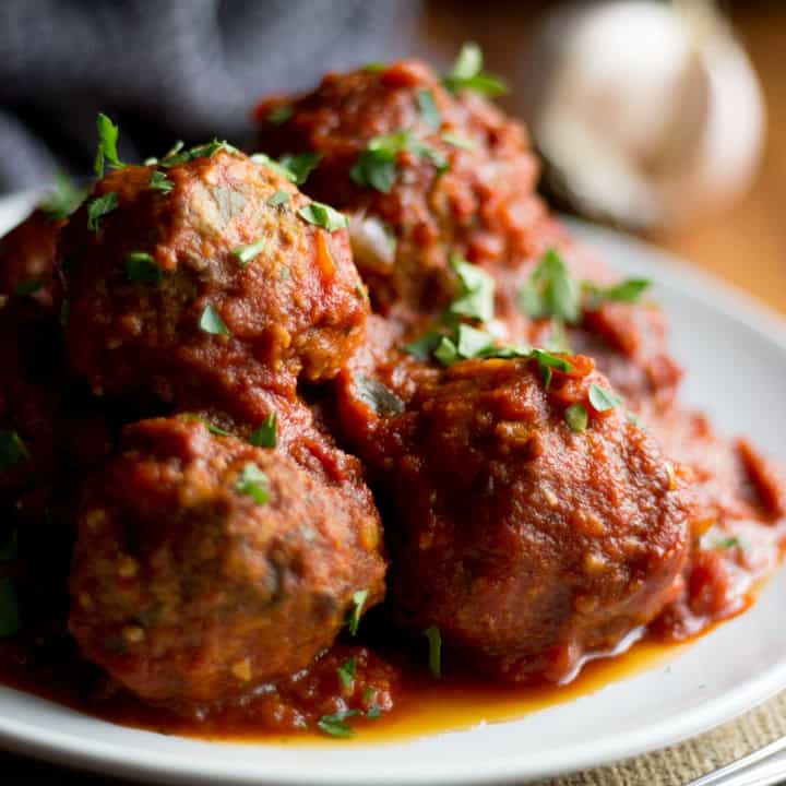 A plate filled with slow cooked meatballs, topped with chopped fresh parsley.