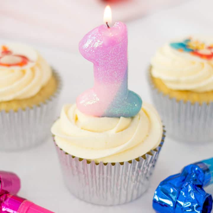 A vanilla cupcake decorated with icing, topped with a large no.1 candle.