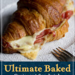 A baked honey mustard glazed gouda and prosciutto croissant sandwich on a plate with a fork. A text overlay says "Ultimate baked croissant sandwich with a honey mustard glaze!"