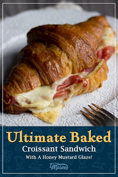 A baked honey mustard glazed gouda and prosciutto croissant sandwich on a plate with a fork. A text overlay says "Ultimate baked croissant sandwich with a honey mustard glaze!"